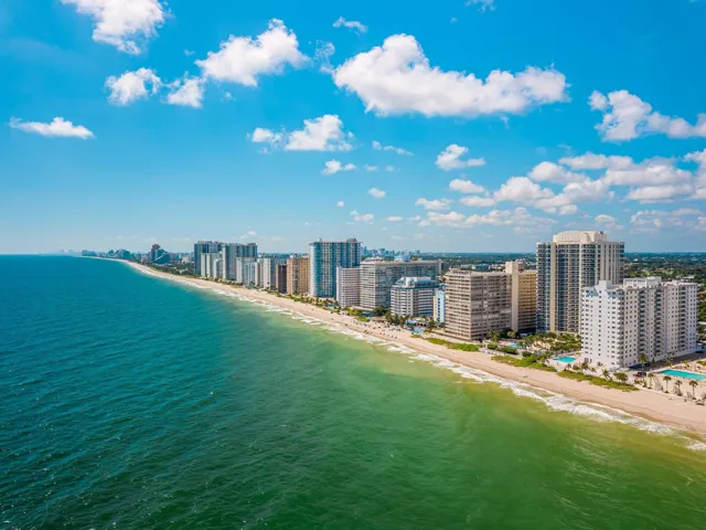 Expansive coastline with multiple high-rise structures, a wide sandy beach, and clear ocean waters