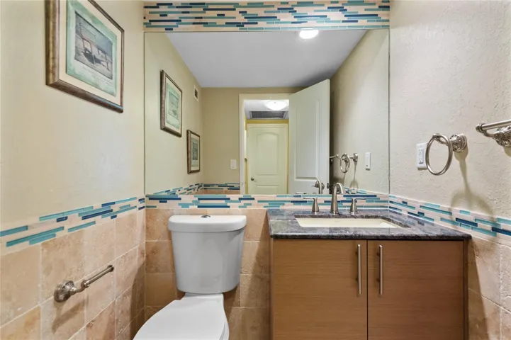 Full-height vanity mirror, stone-finish countertop, undermount sink, wood-finish cabinetry, and decorative tile accent