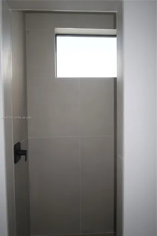 Bathroom 3, Shower enclosure featuring large-format neutral tile, a rectangular transom window, and matte black plumbing fixtures