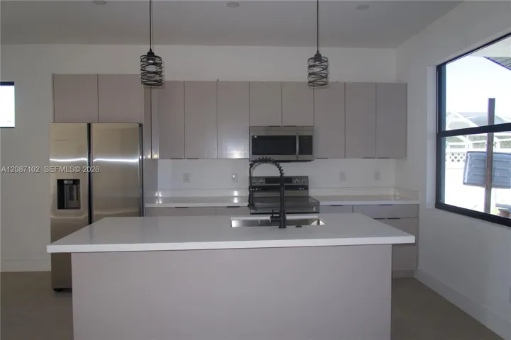 Kitchen featuring flat-panel cabinetry, quartz countertops, a central island with a matte black pull-down faucet, stainless steel appliances, and dual industrial-style pendant lights