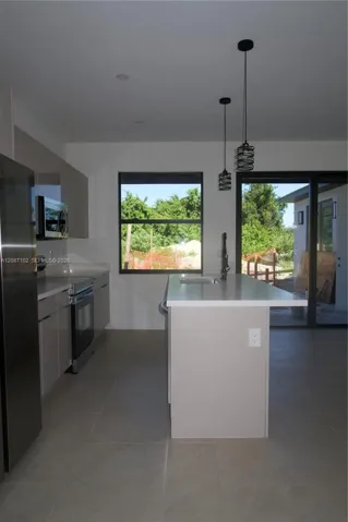 Kitchen featuring flat-panel cabinetry, a central island with an integrated sink, stone-finish countertops, stainless steel appliances, and dual pendant light fixtures
