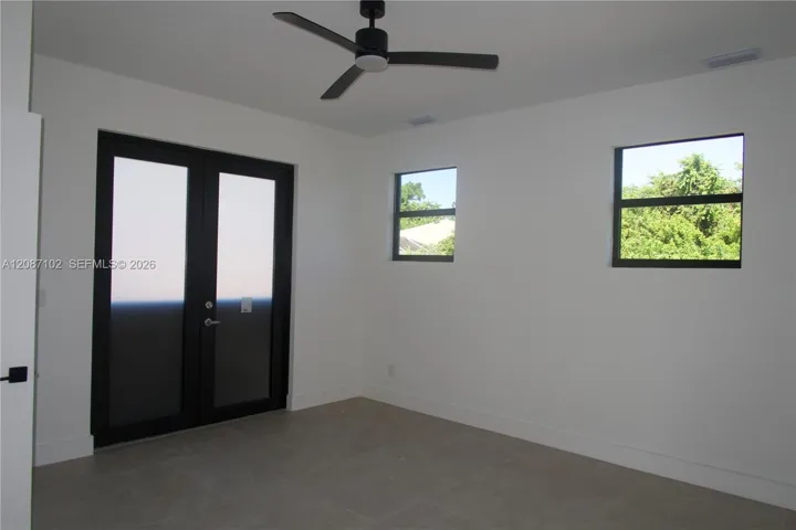 Door leads to pool/outdoor area. Room featuring matte black double French doors, large-format tile flooring, a contemporary three-blade ceiling fan, and black-framed windows