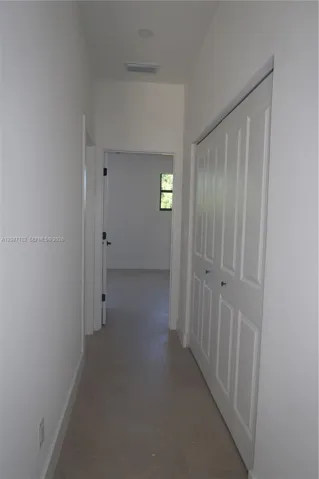 Hallway featuring neutral-tone tile flooring, white panel-style closet doors, recessed lighting, and a doorway with a framed window