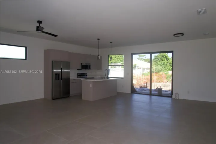 Open-concept kitchen featuring flat-panel cabinetry, a central island with stone-finish countertops, stainless steel appliances, large-format tile flooring, and a sliding glass door