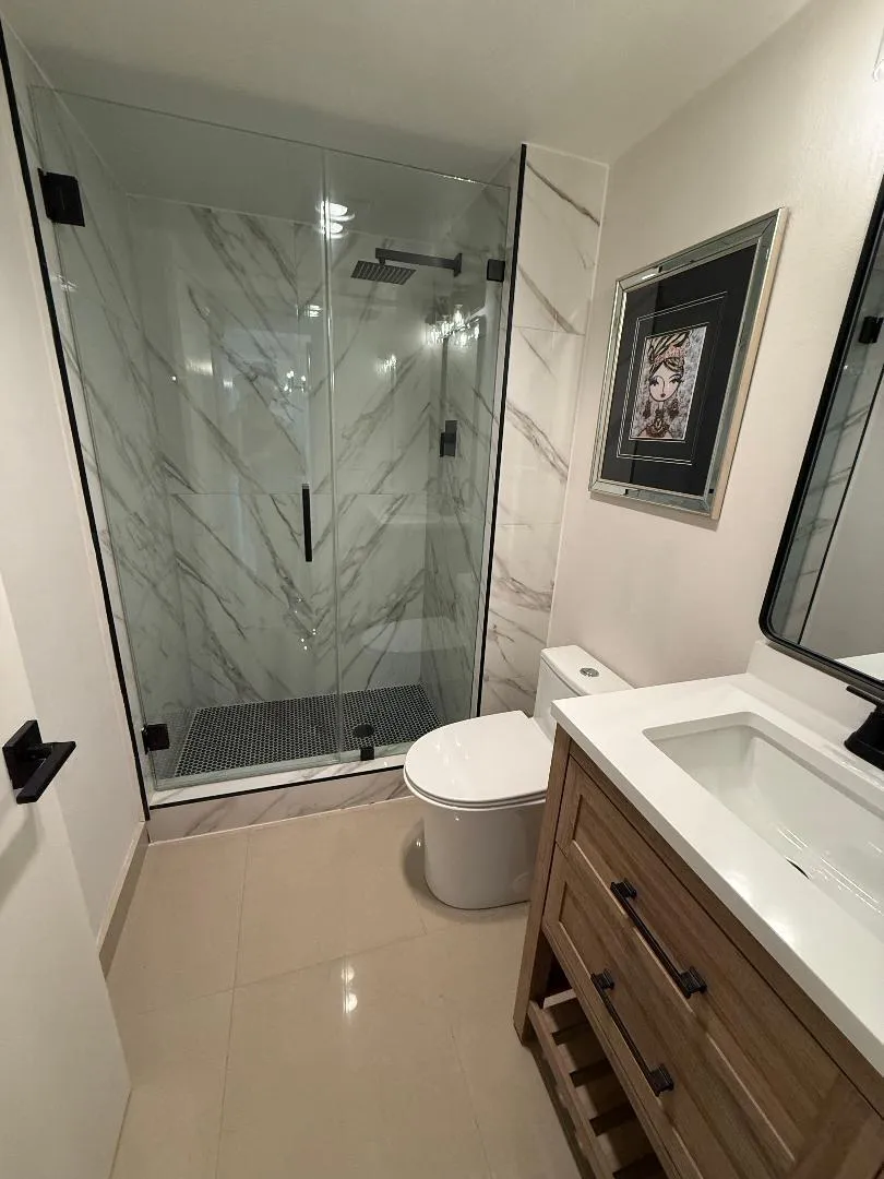 Guest bath with porcelain tile, white oak vanity with quartz countertop. Frameless shower enclosure.