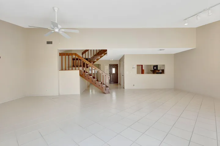 Spacious living area with light tile flooring and a wood staircase, offering an easy flow to the kitchen through a convenient pass-through.