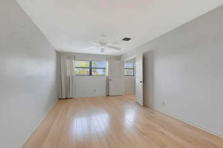 Spacious second-floor primary bedroom with double-door entry, light wood-finish flooring, neutral white walls, and a private ensuite bath.