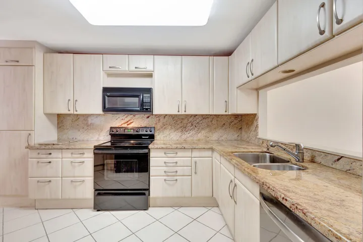Kitchen featuring light wood-finish cabinetry, stone countertops, stainless steel double basin sink, and tile flooring