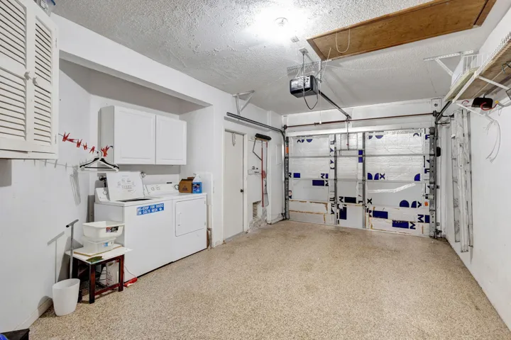 Integrated laundry area with built-in cabinetry, overhead garage door with opener, and a textured concrete floor