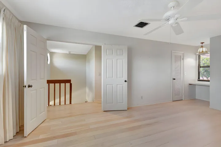 Spacious second-floor primary bedroom with double-door entry, light wood-finish flooring, neutral white walls, and a private ensuite bath.