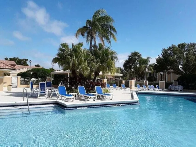 Sparkling blue swimming pool with integrated steps, surrounded by a paved deck, mature palm trees, and lush landscaping