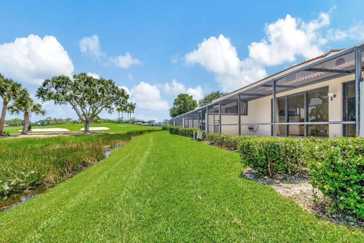 Screened patio enclosure with sliding glass doors, manicured lawn, golf course frontage, and mature landscaping