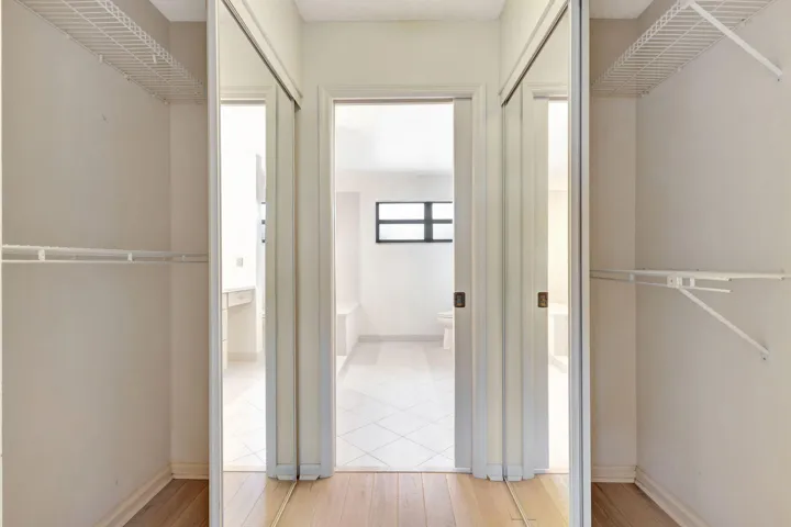 Generous primary walk-in closet with wood-finish flooring and mirrored sliding doors, offering ample storage space.