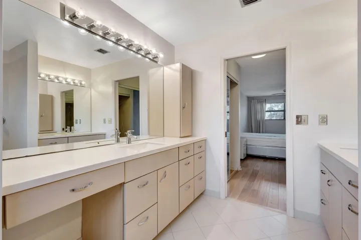 Expansive vanity with dual sinks, extensive storage cabinetry, a dedicated dressing area, and a large wall-mounted mirror with overhead lighting