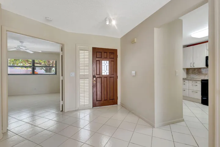 Entryway with tile flooring, a paneled wood entry door, and interior plantation shutters