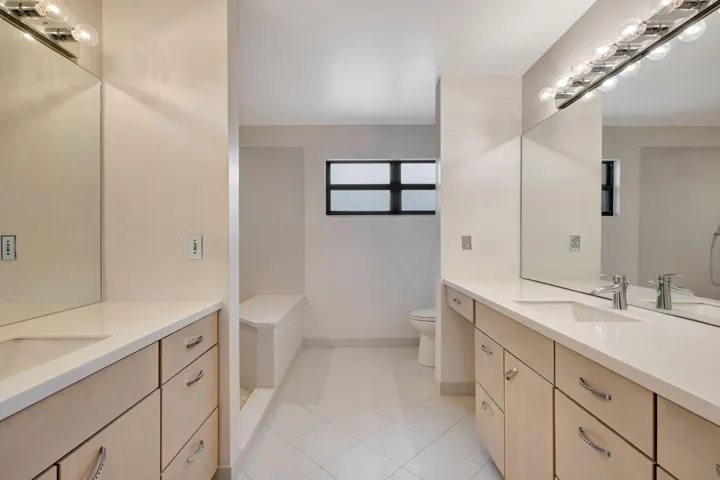 Spacious primary bath with a double vanity, undermount sinks, and warm light wood-finish cabinetry.