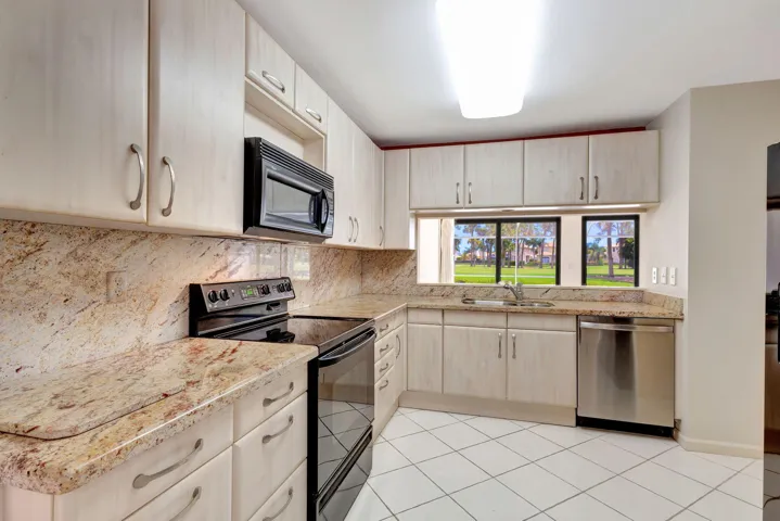 Kitchen featuring light wood-finish cabinetry, patterned stone countertops, a full-size range, stainless steel dishwasher, and tile flooring