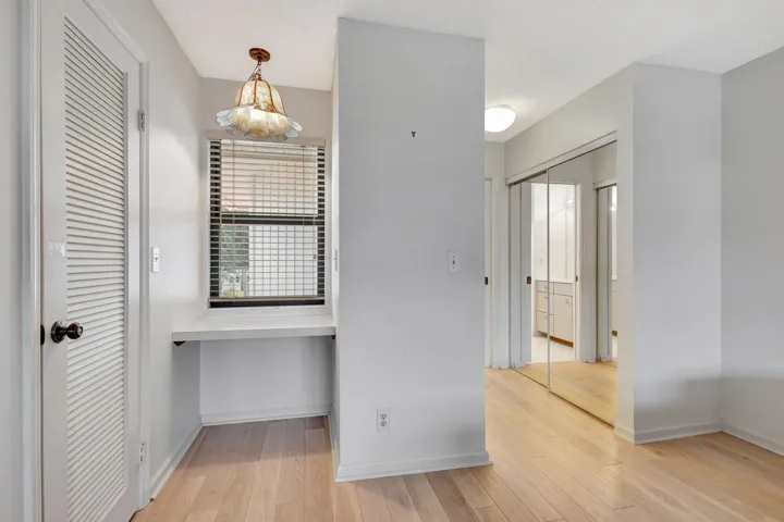Light wood-finish flooring, built-in desk, window with blinds, louvered door, mirrored closet doors