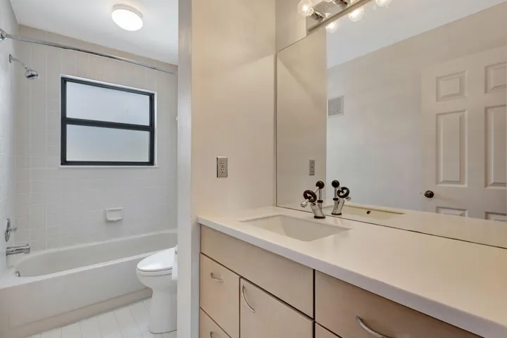 Bright guest bathroom featuring a vanity with integrated sink, light wood-finish cabinetry, chrome hardware, and a relaxing tub.