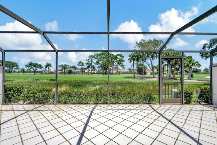 Screened patio with diagonal tile flooring, a screened door, and a natural grass and tree landscape beyond