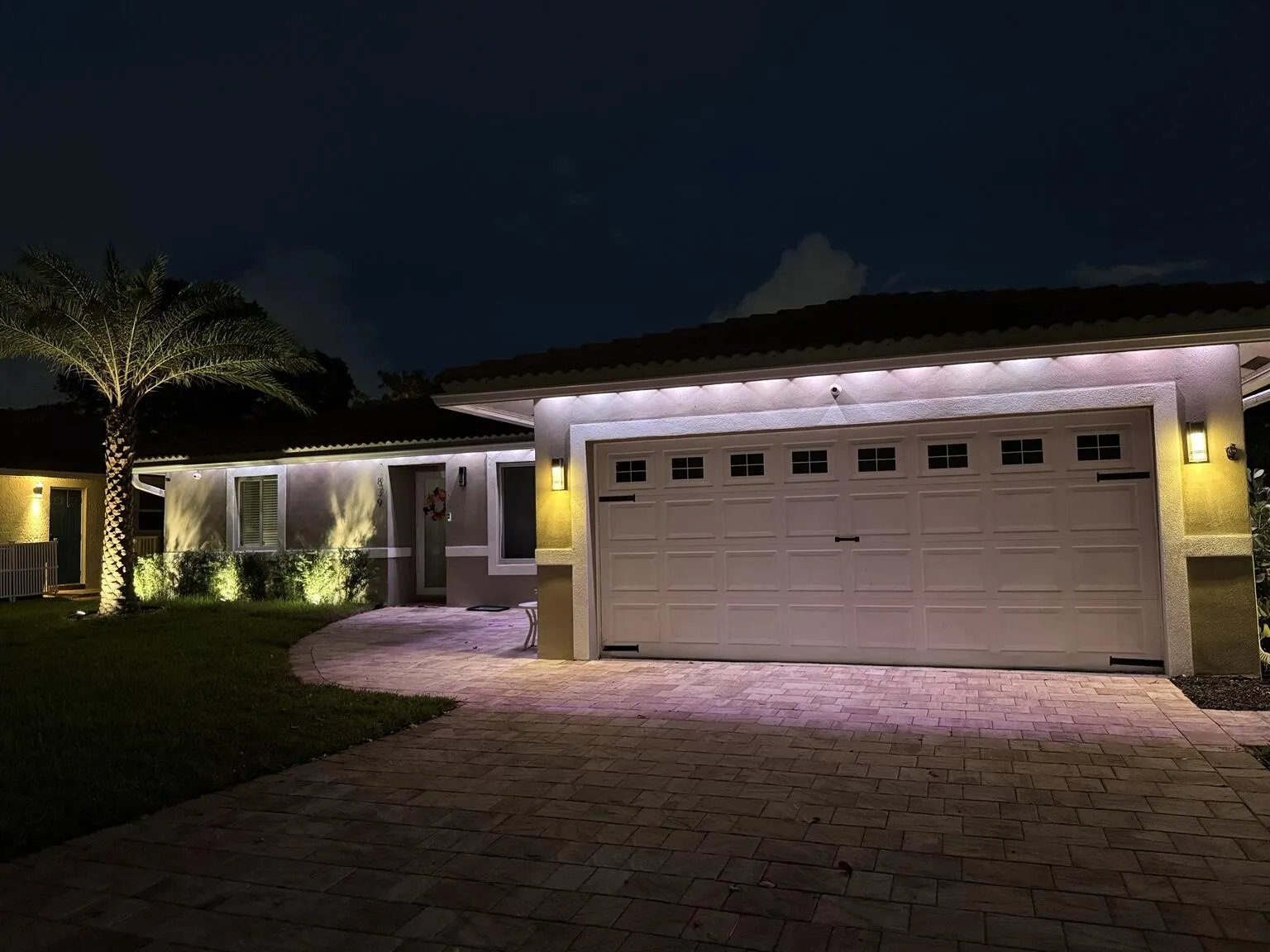 Paver driveway leading to a two-car garage with decorative windows and sconce lighting