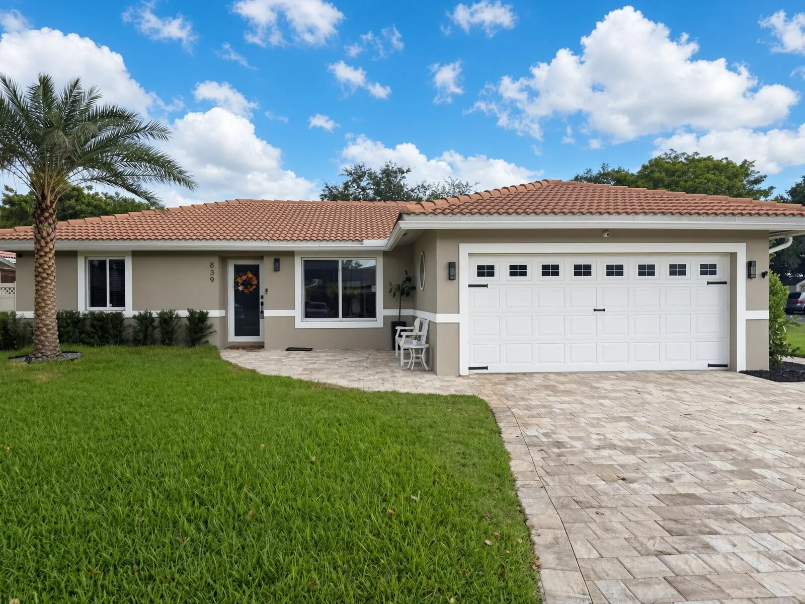 Stucco exterior with a tile roof, paver driveway, and a two-car garage with decorative hardware