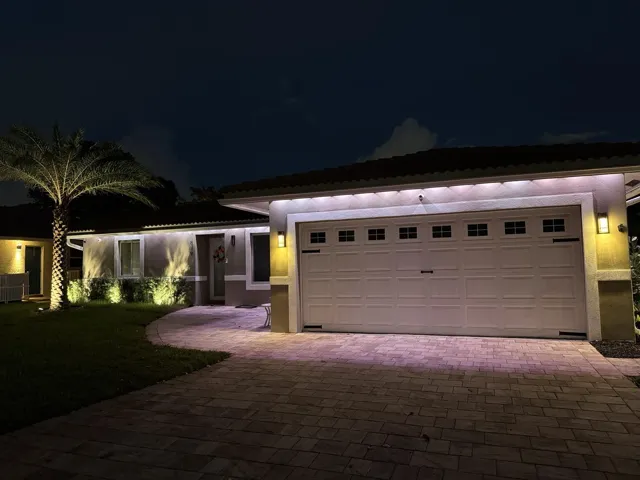 Paver driveway leading to a two-car garage with decorative windows and sconce lighting