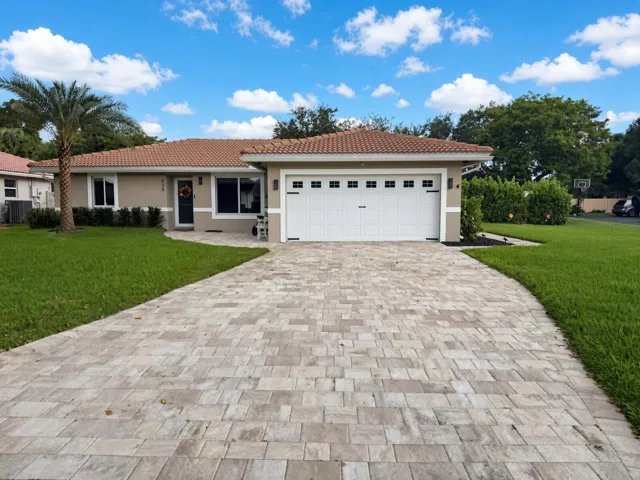 Tiled roof residence with a paver driveway, an attached garage, a mature palm, and exterior landscaping