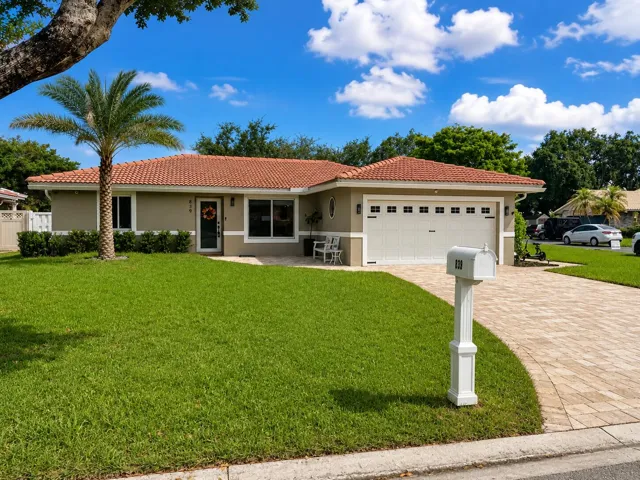 Mediterranean-style roof tiles, stucco exterior, attached garage, paver driveway, and mature landscaping