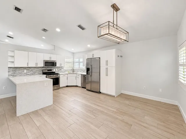 Modern kitchen featuring stainless steel appliances, white cabinetry, a large kitchen island with a light-colored countertop, a mosaic tile backsplash, and light wood-finish flooring