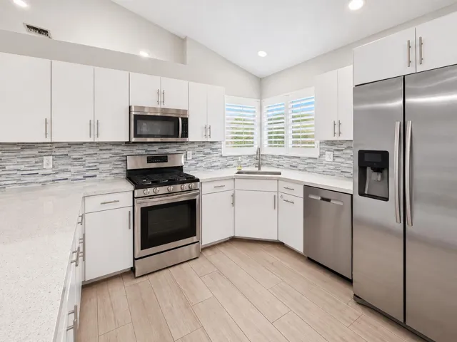 Kitchen featuring white cabinetry, stone countertops, stainless steel appliances, a mosaic tile backsplash, and wood-finish flooring