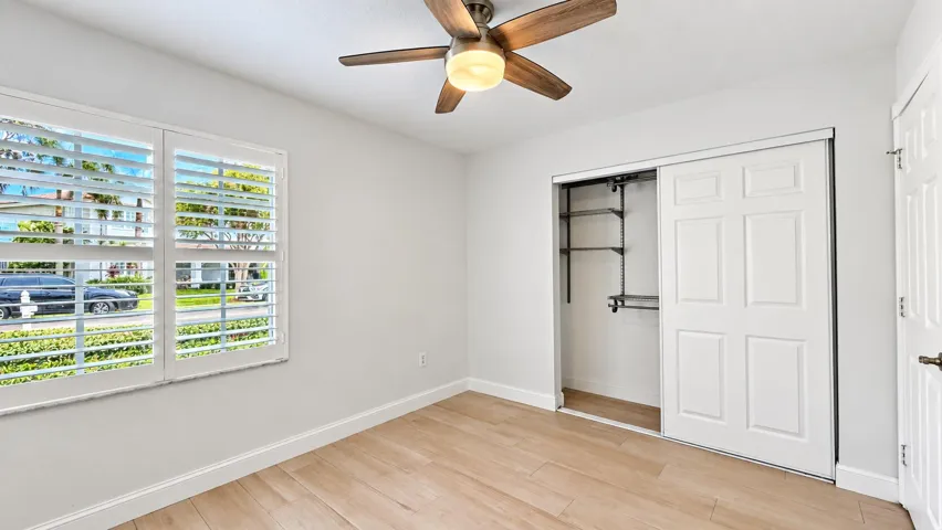 Plantation shutters, wood-finish flooring, ceiling fan with light fixture, sliding closet doors, and built-in closet shelving