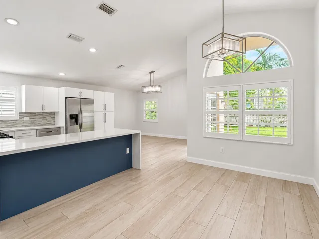 Open-concept dining space with wood-finish flooring, a kitchen island with a solid surface countertop, stainless steel appliances, and a vaulted ceiling with an arched window