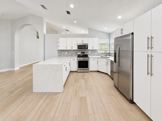 Kitchen featuring a substantial island with a light-toned countertop, stainless steel appliances, white cabinetry, a tiled backsplash, and wood-finish flooring