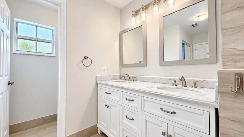 Dual vanity with white cabinetry, integrated sinks, brushed nickel fixtures, and a marble-finish countertop
