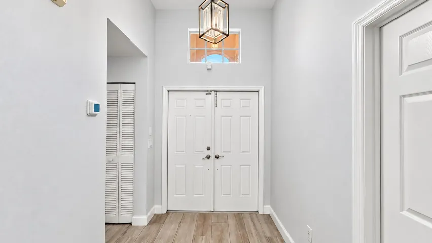 Double-door entry with transom window, vaulted ceiling, and wood-finish flooring