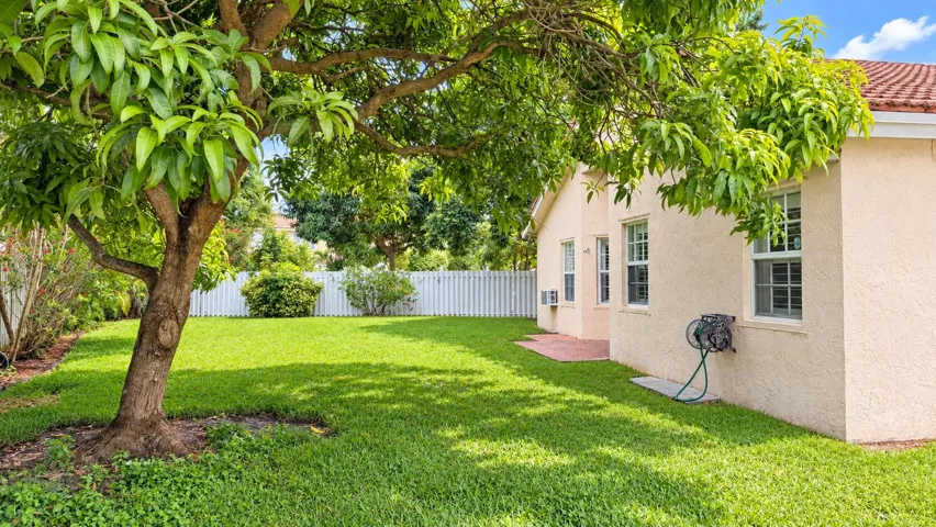 Expansive green lawn featuring mature trees, a stucco exterior, multiple windows, and a partial privacy fence