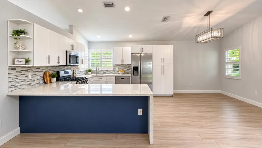 Gourmet kitchen featuring a peninsula with a light-colored countertop, white cabinetry with silver-tone hardware, stainless steel appliances, and a mosaic tile backsplash