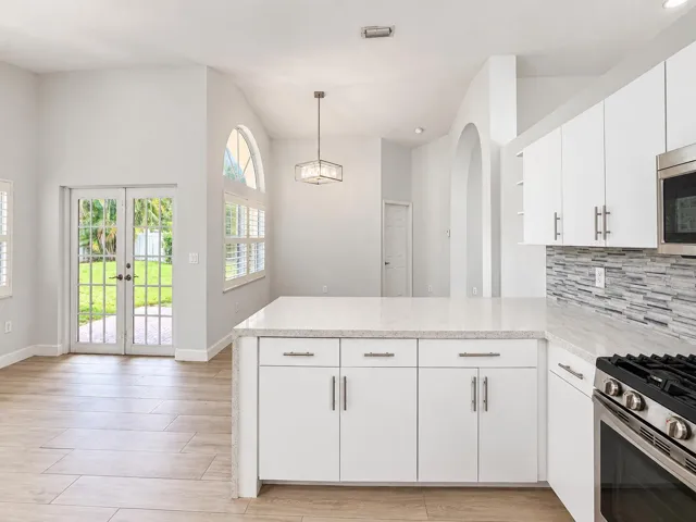 Vaulted ceiling with a contemporary chandelier, white shaker cabinetry, stone countertops, and a mosaic tile backsplash