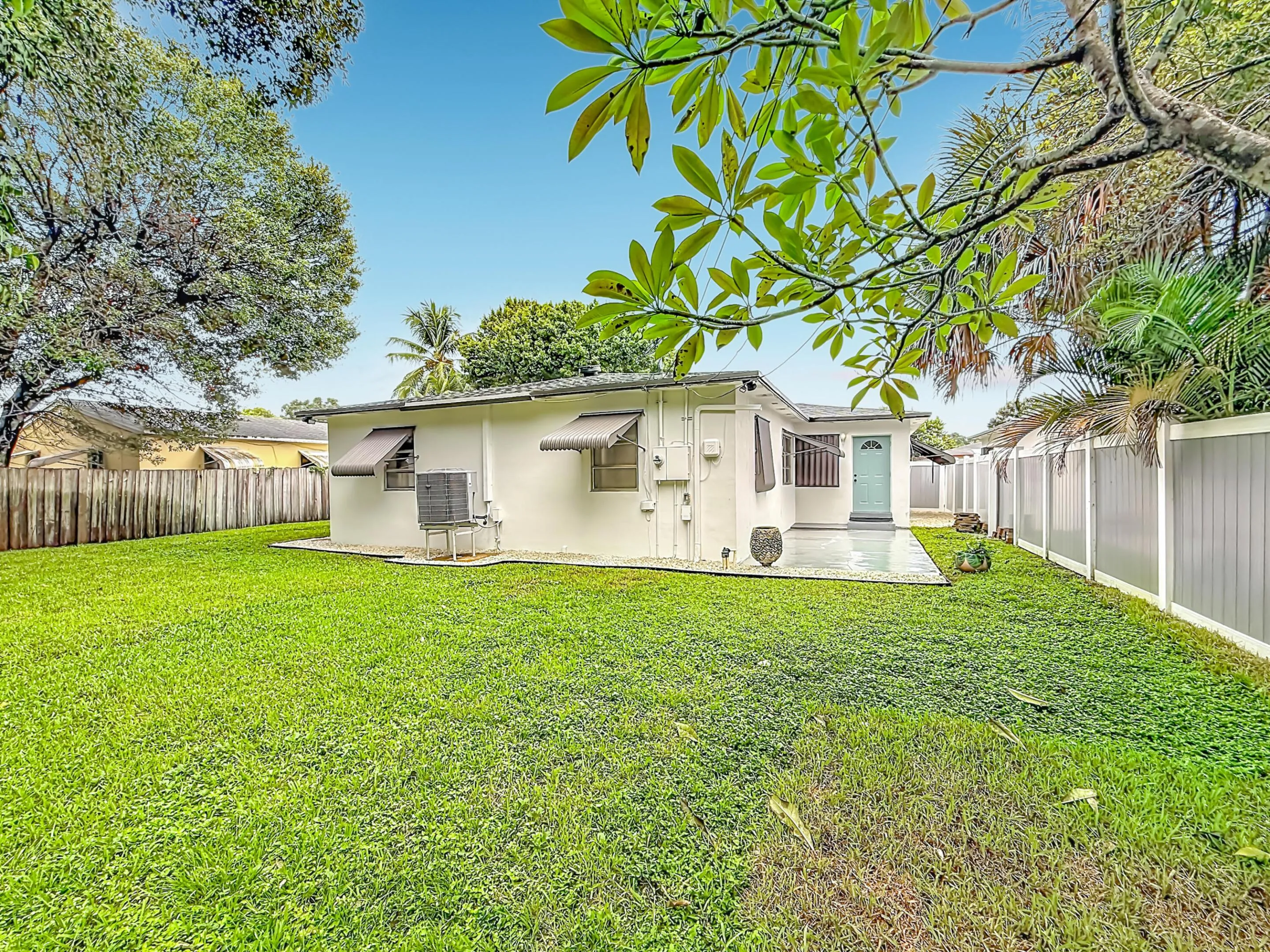 Expansive lawn with perimeter fencing, rear patio space, and exterior window awnings
