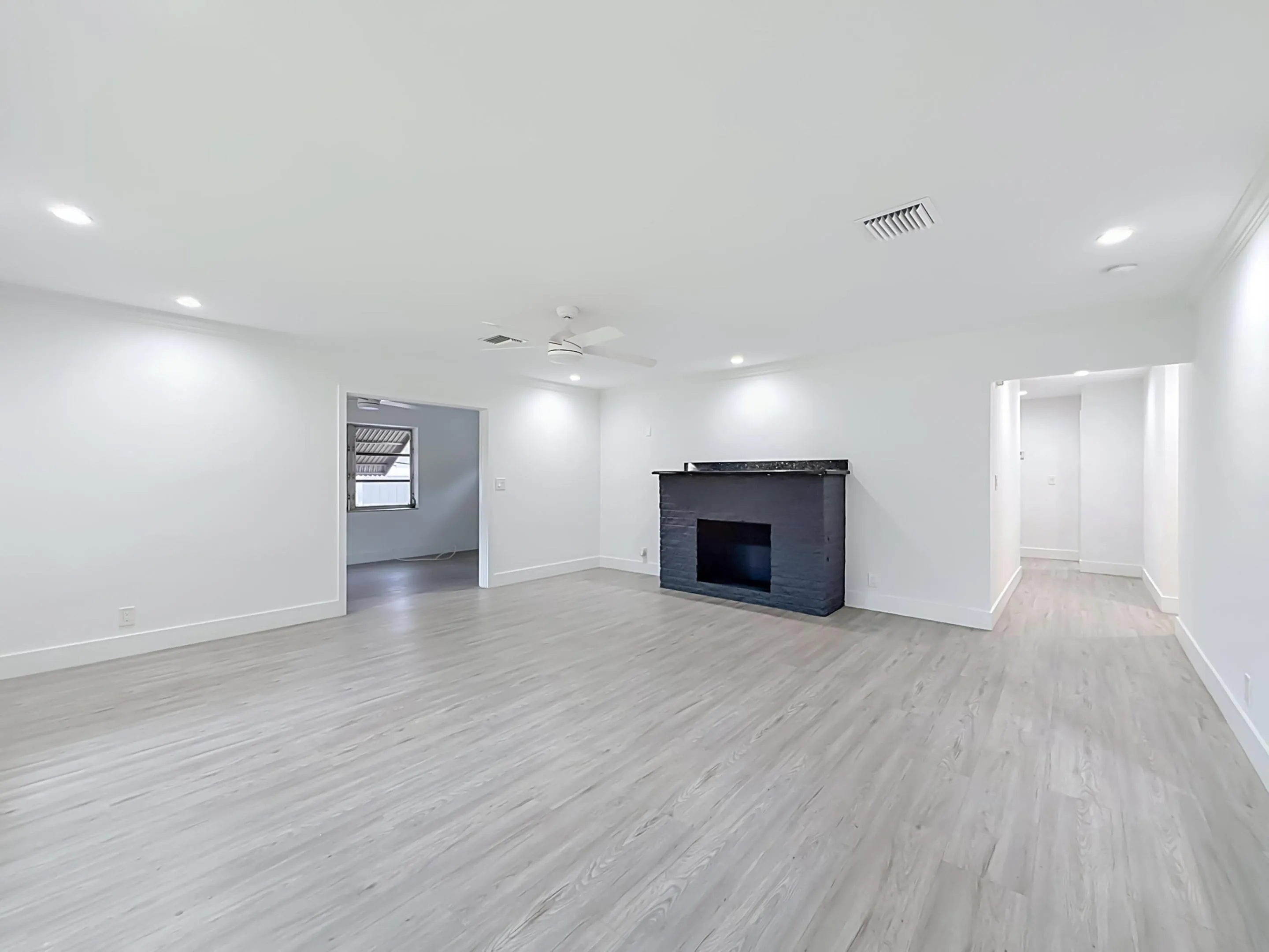 Spacious interior with light wood-finish flooring, recessed lighting, ceiling fan, and a painted fireplace with a dark stone-finish mantel