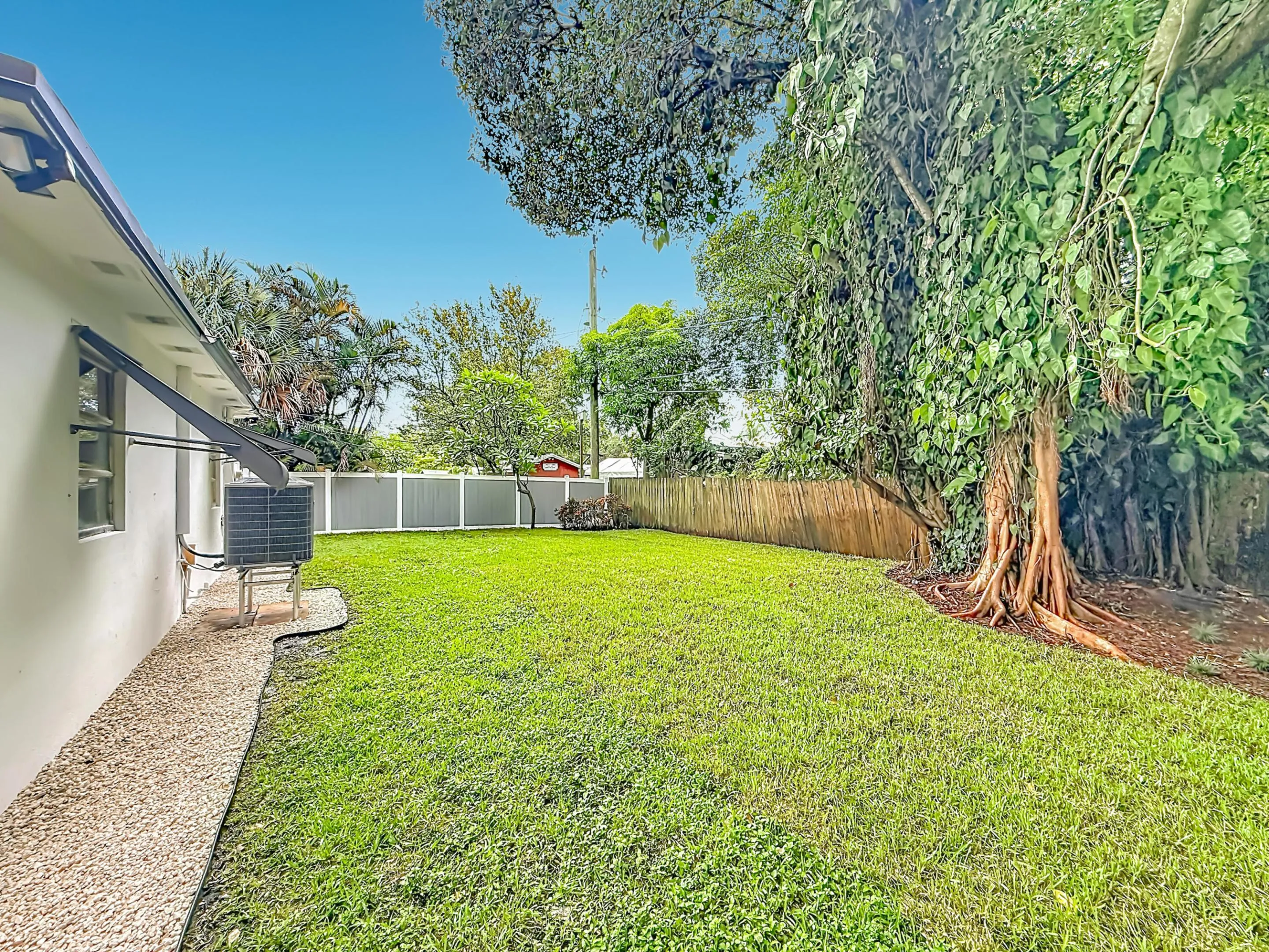 Expansive green lawn with mature trees, fenced perimeter, and gravel landscaping along the exterior wall