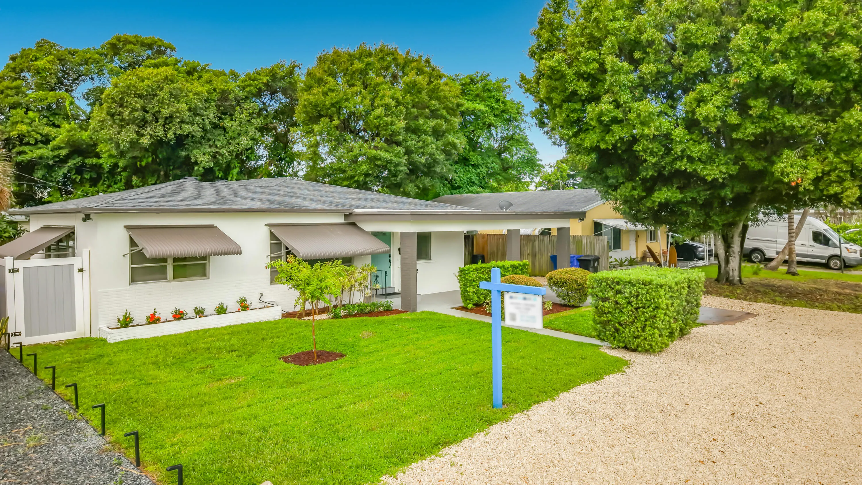 White stucco exterior with a dark shingle roof, complemented by window awnings