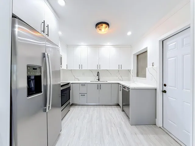Updated kitchen featuring stainless steel appliances, two-tone cabinetry, quartz countertops with matching backsplash, and wood-finish flooring