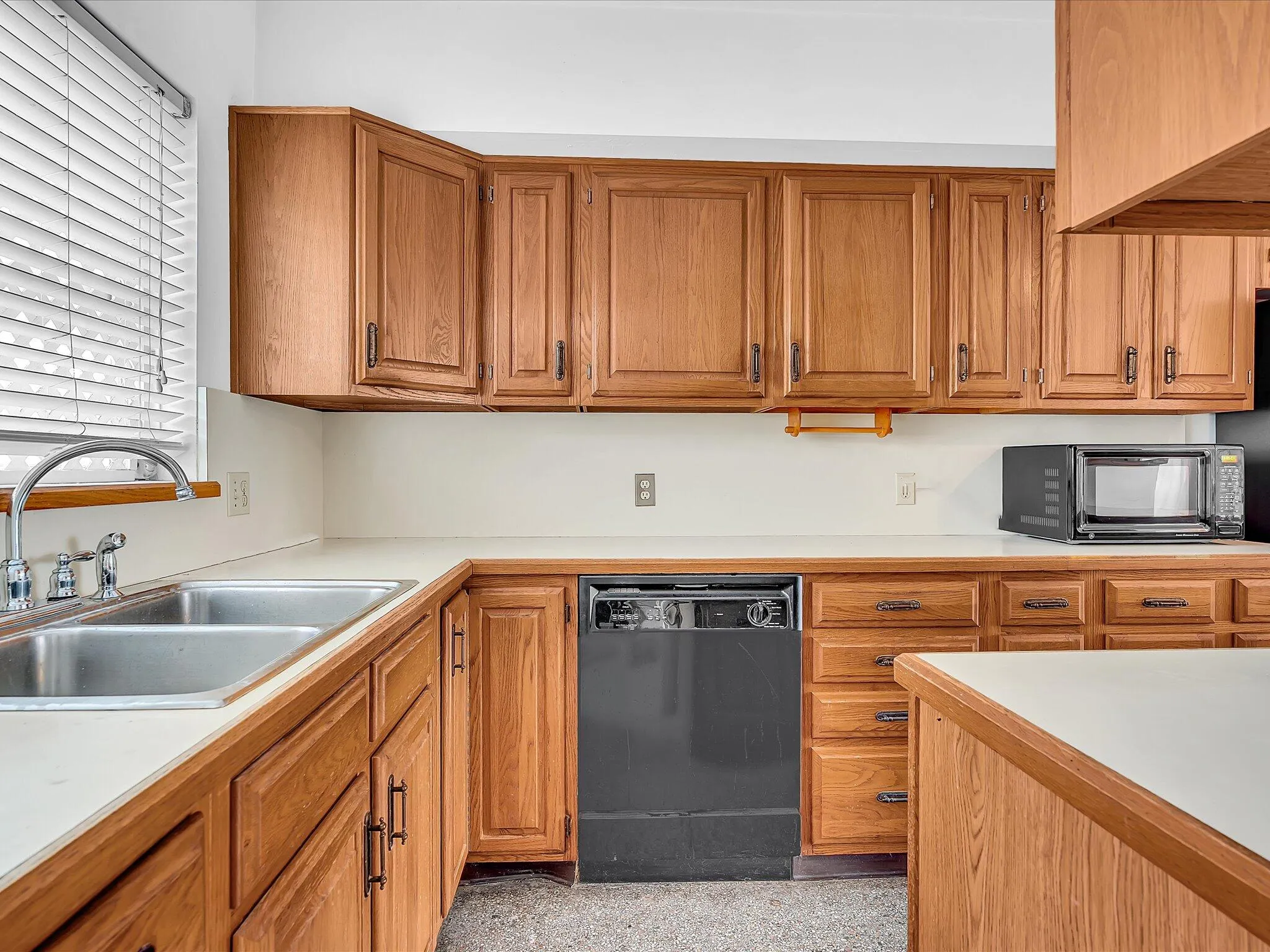 Wood-finish cabinetry with coordinating hardware, dual basin stainless steel sink, and light-toned countertops