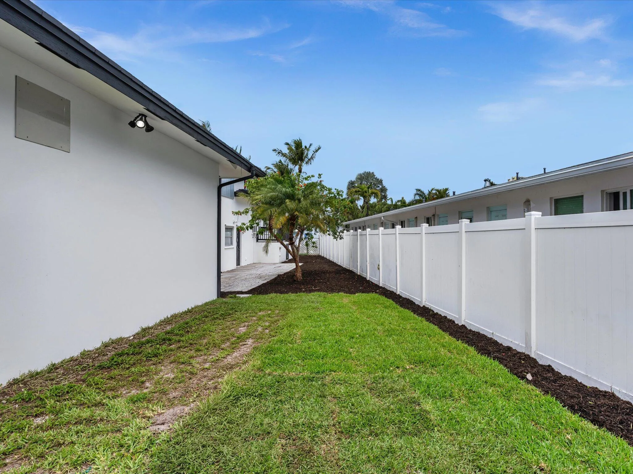 Expansive lawn area bordered by a white privacy fence and a building with a dark-trimmed roofline and exterior lighting