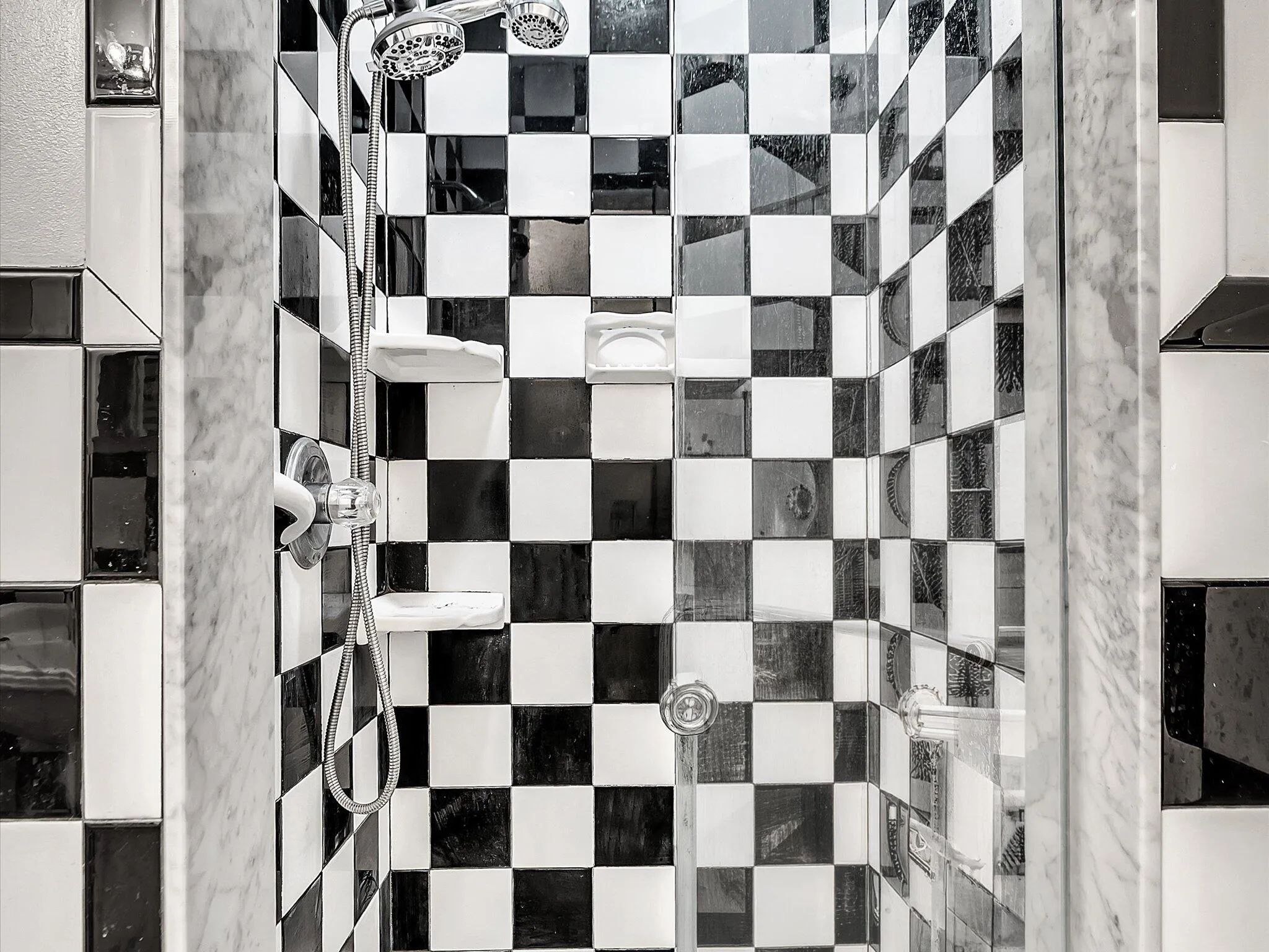Shower enclosure with checkerboard tile, chrome showerhead, and integrated shelving