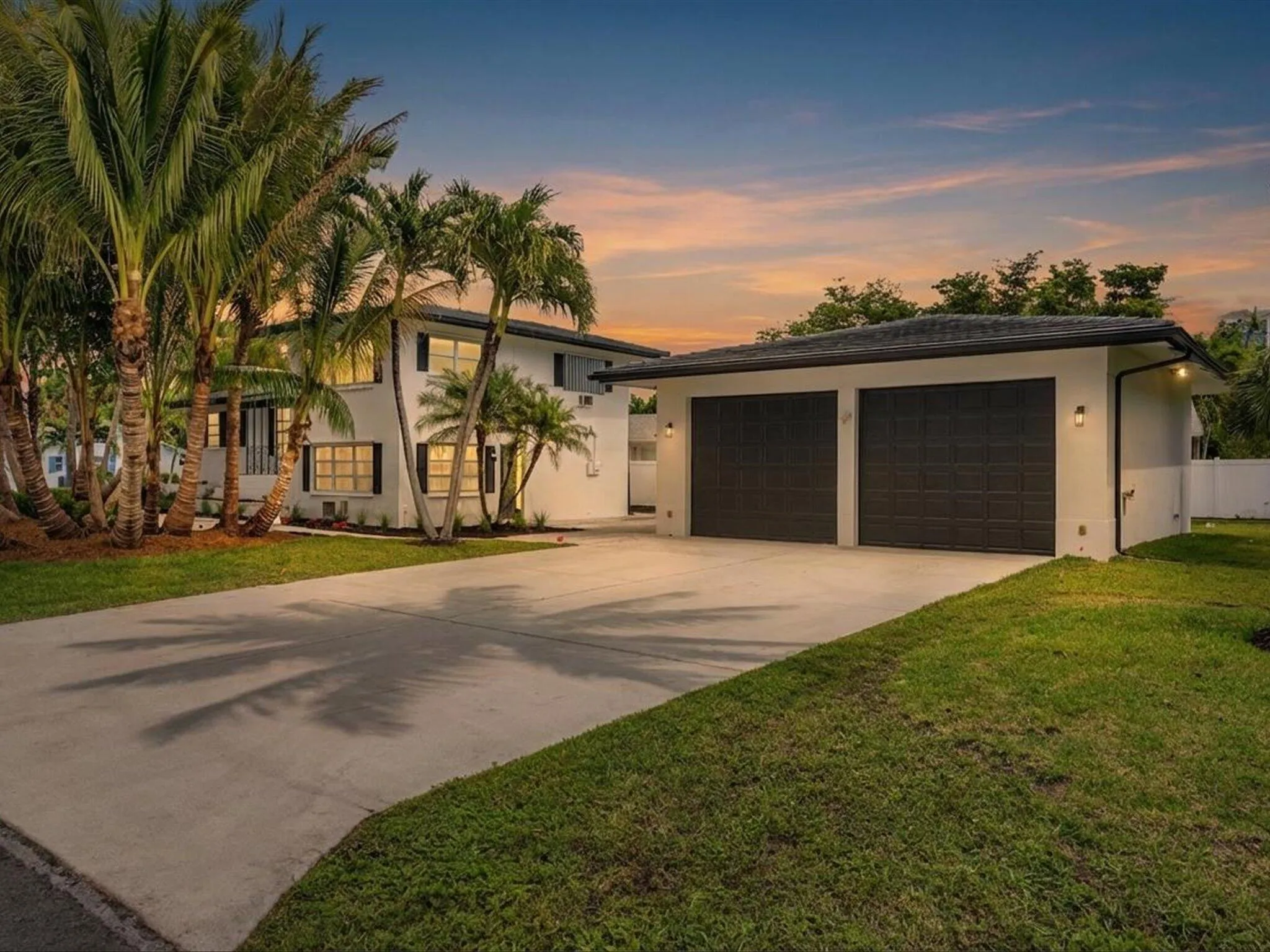 Contemporary-style residence with a two-car garage, concrete driveway, and established palm trees