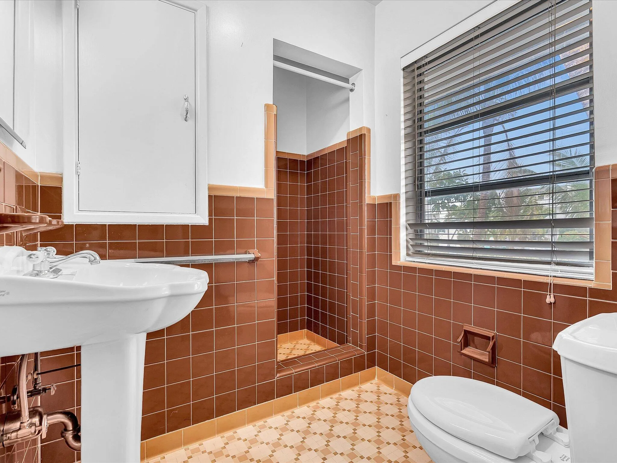 Bathroom featuring a pedestal sink, tiled shower, built-in wall cabinet, and window with blinds