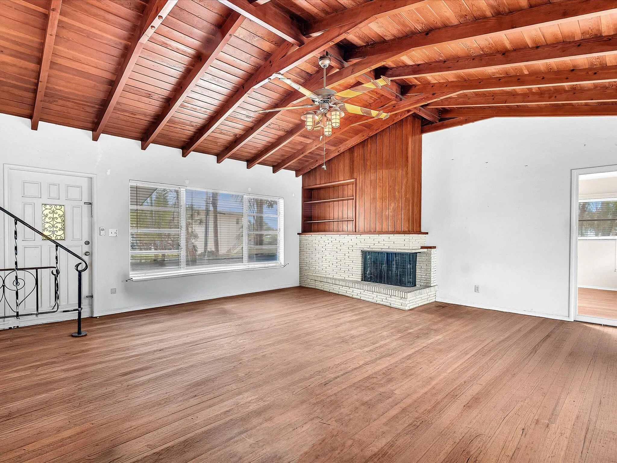 Vaulted wood-paneled ceiling, wood-finish flooring, built-in fireplace with brick surround, built-in shelving, and multiple windows